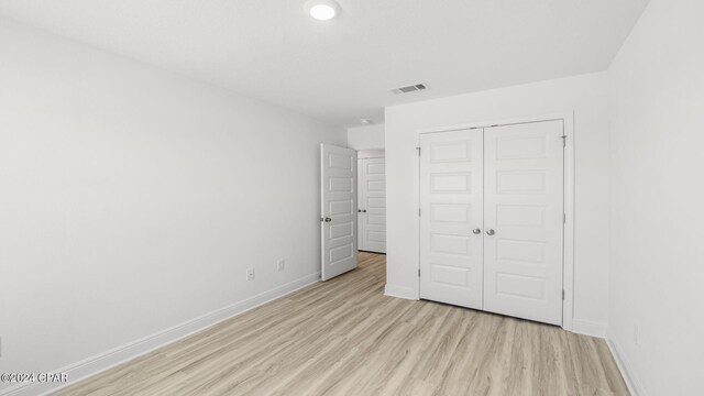 unfurnished bedroom with a closet, visible vents, light wood-style floors, and baseboards