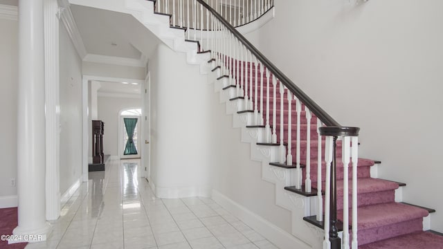 stairs with crown molding, a towering ceiling, baseboards, and decorative columns