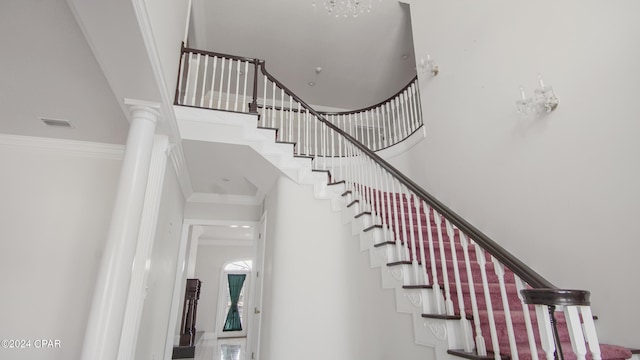 staircase featuring decorative columns, a high ceiling, ornamental molding, and visible vents