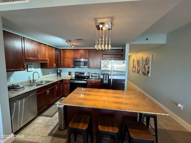 kitchen with hanging light fixtures, sink, stainless steel appliances, a kitchen breakfast bar, and a center island