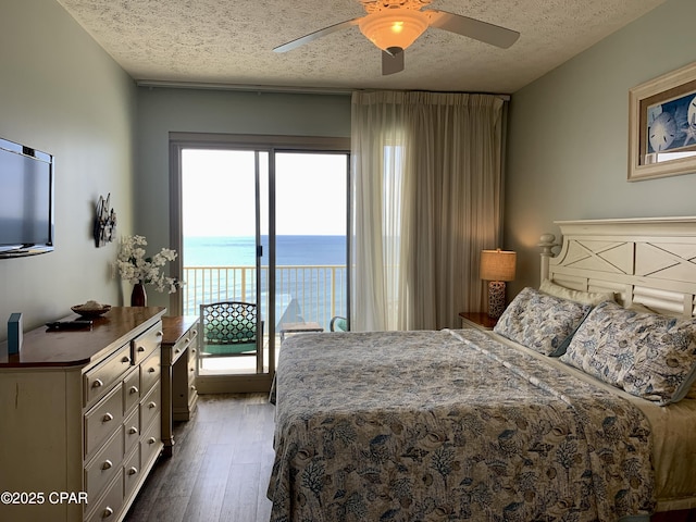 bedroom with ceiling fan, access to exterior, a water view, a textured ceiling, and dark hardwood / wood-style flooring