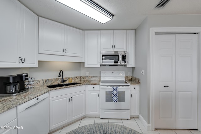 kitchen featuring white appliances, a textured ceiling, sink, light tile patterned floors, and white cabinetry