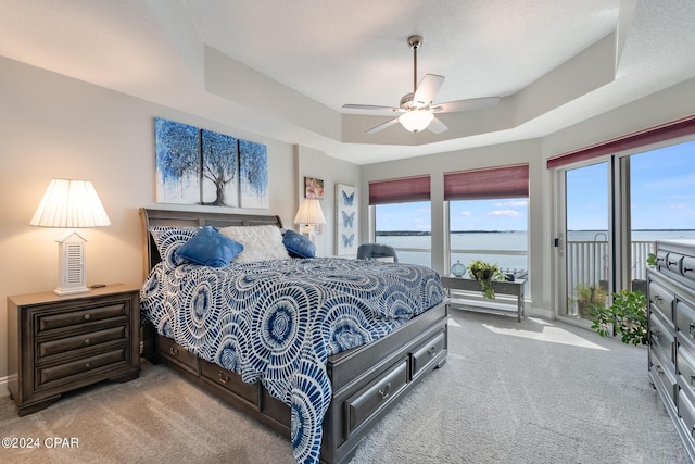 bedroom with light carpet, a water view, ceiling fan, and a tray ceiling