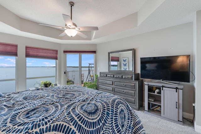 bedroom featuring a textured ceiling, access to outside, light colored carpet, ceiling fan, and a tray ceiling