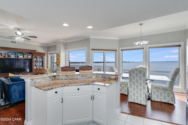 kitchen with a center island, a water view, hanging light fixtures, white cabinetry, and wood-type flooring