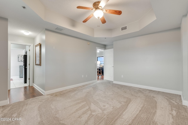 carpeted spare room featuring a textured ceiling, a tray ceiling, and ceiling fan