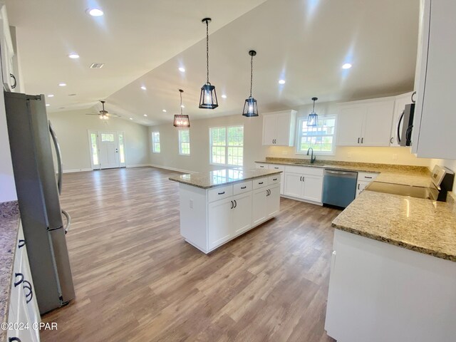 kitchen featuring a kitchen island, white cabinets, open floor plan, appliances with stainless steel finishes, and light stone countertops