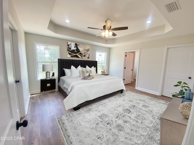 bedroom with dark wood-style floors, baseboards, visible vents, and a raised ceiling