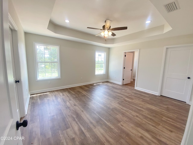 unfurnished bedroom with a raised ceiling, visible vents, baseboards, and wood finished floors