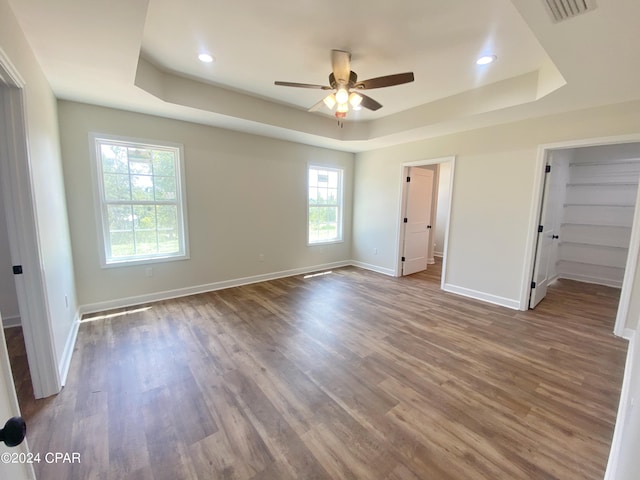 unfurnished bedroom with wood finished floors, visible vents, baseboards, a spacious closet, and a tray ceiling