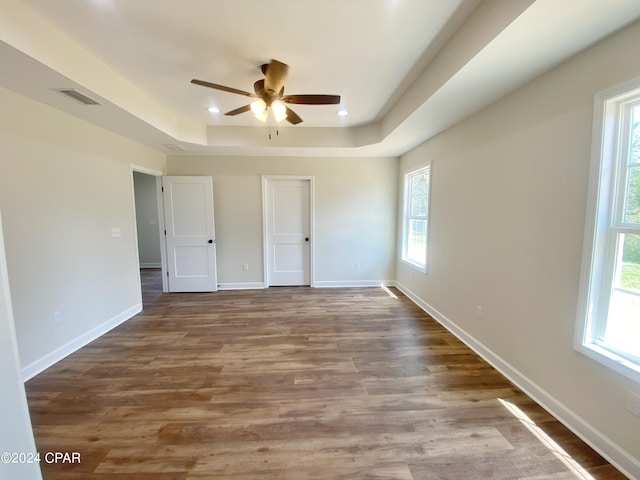 unfurnished bedroom with baseboards, visible vents, a tray ceiling, and wood finished floors