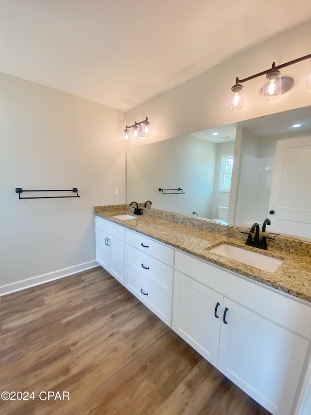 full bath with double vanity, wood finished floors, a sink, and toilet