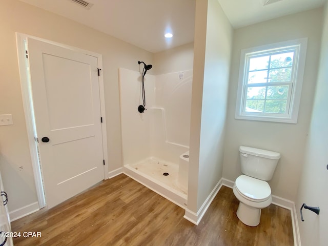 bathroom with a stall shower, wood finished floors, toilet, and baseboards