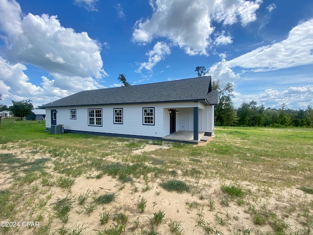 rear view of house featuring central AC unit, a lawn, board and batten siding, and roof with shingles