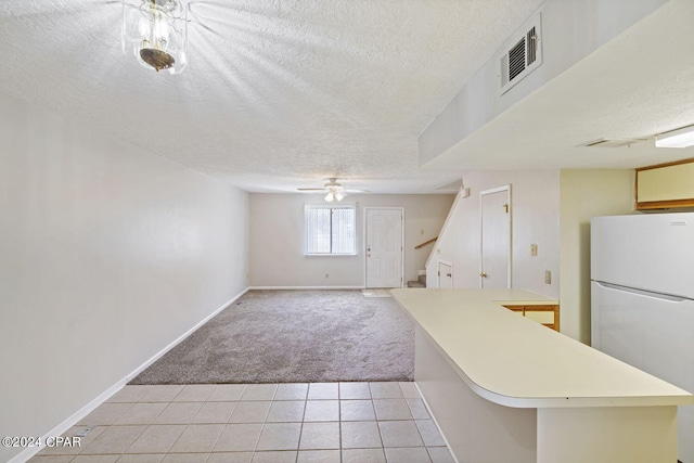 kitchen with white fridge, a textured ceiling, kitchen peninsula, and light colored carpet