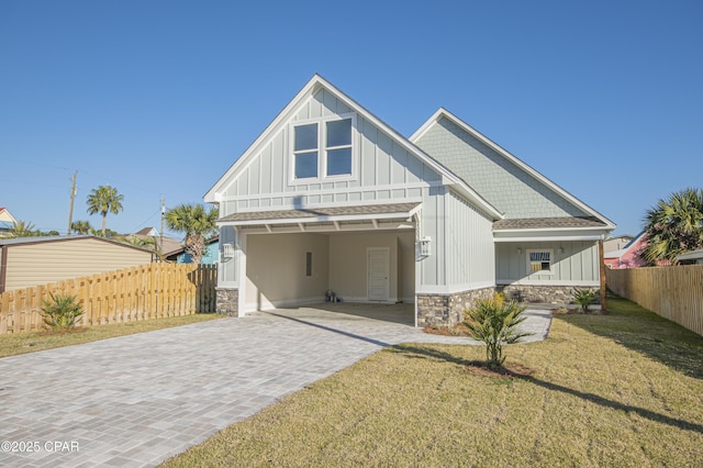 back of house featuring decorative driveway, a lawn, board and batten siding, and stone siding