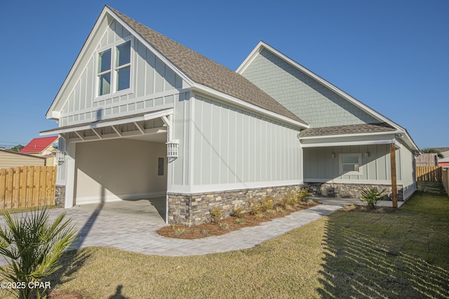 back of property with stone siding, a lawn, roof with shingles, and fence