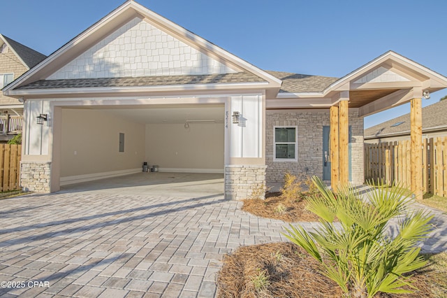 craftsman inspired home with fence, an attached garage, a shingled roof, stone siding, and decorative driveway