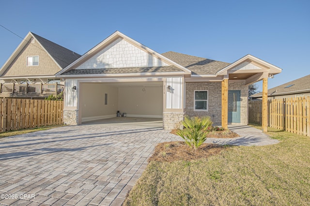 view of front of house with decorative driveway, stone siding, fence, an attached garage, and a shingled roof