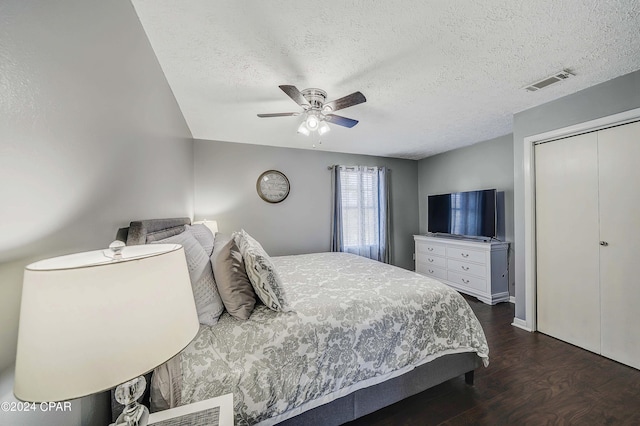 bedroom with a textured ceiling, dark wood-type flooring, ceiling fan, and a closet