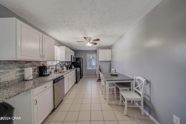 kitchen with white cabinets, appliances with stainless steel finishes, light stone counters, sink, and ceiling fan