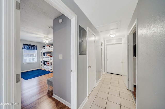 hall with light wood-type flooring, electric panel, and a textured ceiling