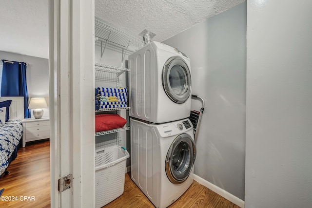 washroom featuring a textured ceiling, hardwood / wood-style floors, and stacked washer and dryer