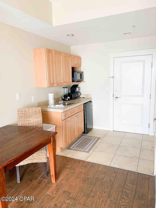 kitchen featuring black appliances, light brown cabinetry, light wood-type flooring, and sink