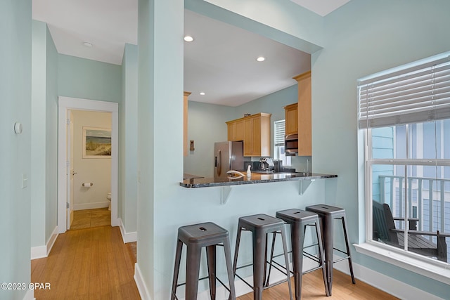 kitchen featuring stainless steel appliances, a breakfast bar area, light hardwood / wood-style flooring, kitchen peninsula, and dark stone counters