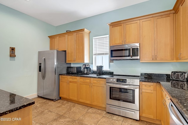 kitchen featuring stainless steel appliances, light tile patterned floors, and dark stone counters