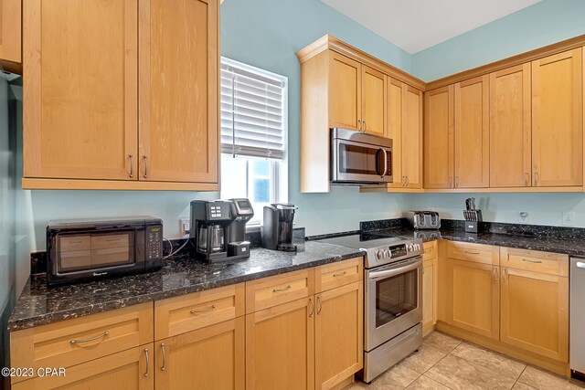 kitchen featuring appliances with stainless steel finishes, light tile patterned floors, and dark stone counters