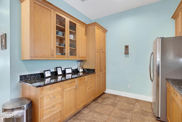 kitchen with dark stone counters, stainless steel fridge, and light brown cabinets