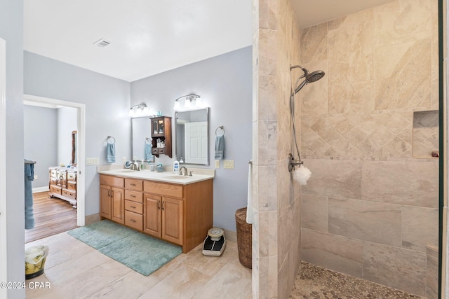 bathroom with vanity with extensive cabinet space, tile floors, a tile shower, and double sink