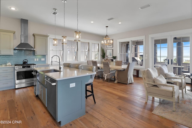 kitchen featuring light hardwood / wood-style floors, decorative light fixtures, appliances with stainless steel finishes, wall chimney exhaust hood, and backsplash