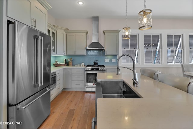 kitchen with appliances with stainless steel finishes, light hardwood / wood-style floors, wall chimney range hood, tasteful backsplash, and pendant lighting