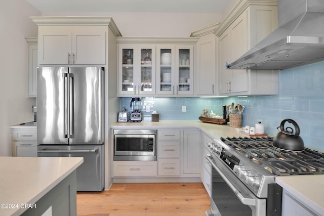 kitchen featuring premium appliances, light hardwood / wood-style floors, white cabinets, tasteful backsplash, and wall chimney exhaust hood