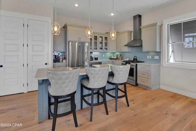 kitchen featuring light hardwood / wood-style floors, decorative light fixtures, stainless steel appliances, and wall chimney range hood