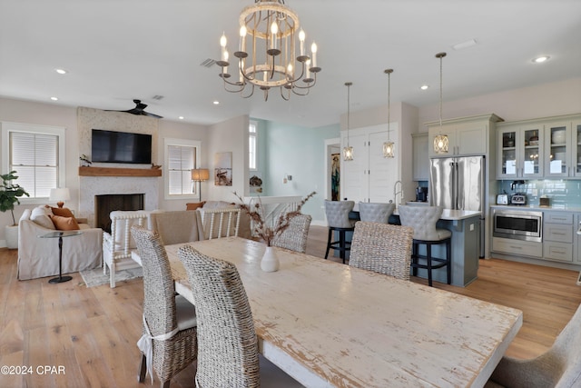 dining area featuring light hardwood / wood-style floors, ceiling fan with notable chandelier, a healthy amount of sunlight, and a fireplace