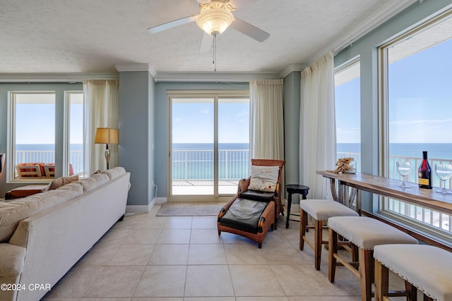 tiled living room featuring ornamental molding, a textured ceiling, ceiling fan, and a water view