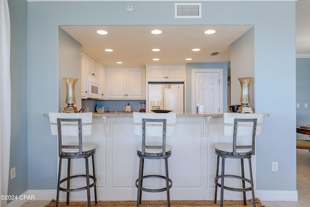 kitchen featuring white appliances, white cabinets, and a kitchen breakfast bar