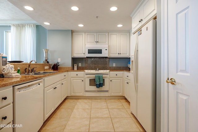 kitchen with light tile floors, kitchen peninsula, white appliances, white cabinets, and sink