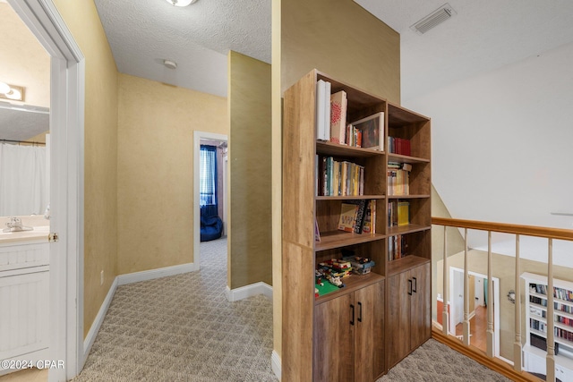 hallway featuring a textured ceiling, light colored carpet, a sink, visible vents, and baseboards