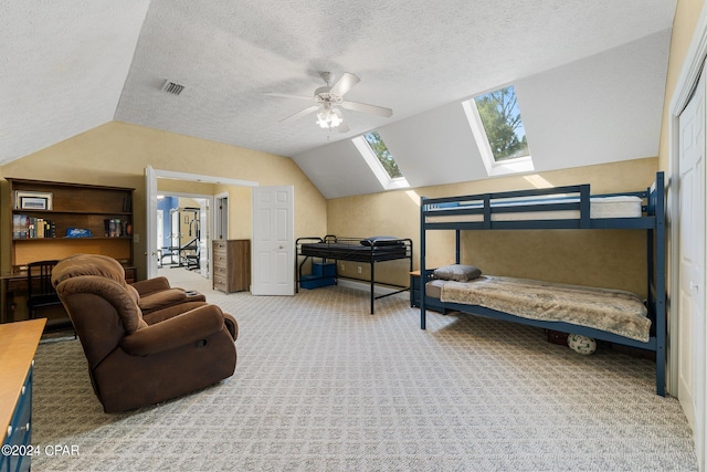 carpeted bedroom featuring lofted ceiling with skylight, visible vents, a textured ceiling, and a ceiling fan