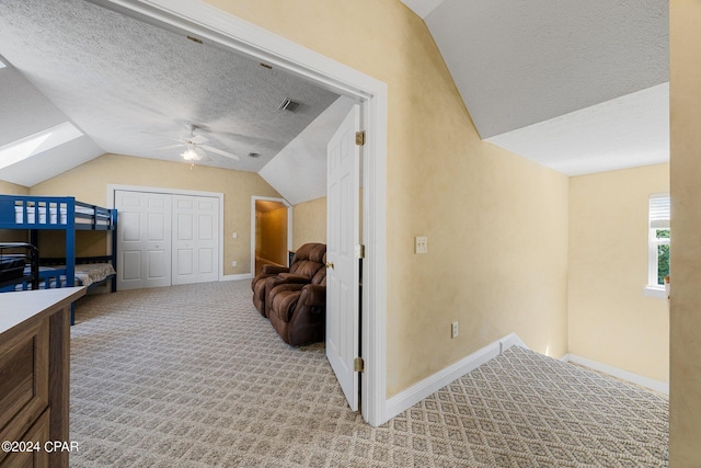 interior space with baseboards, visible vents, light colored carpet, vaulted ceiling, and a textured ceiling