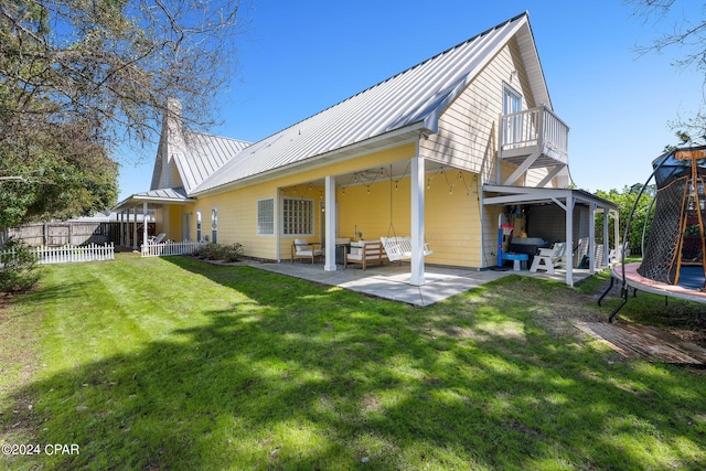 rear view of property featuring a trampoline, fence, a lawn, a standing seam roof, and a patio area