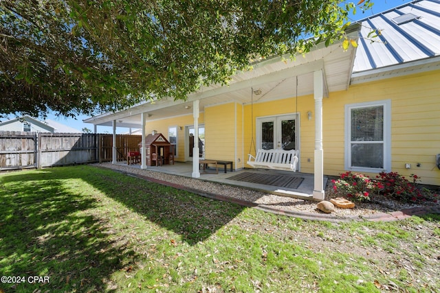 back of property featuring fence, metal roof, a lawn, and a patio