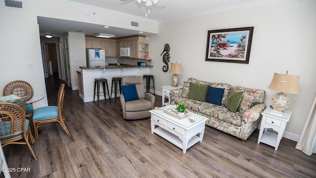 living area with crown molding, wood finished floors, visible vents, and baseboards