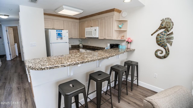 kitchen featuring a breakfast bar, wood finished floors, white appliances, a peninsula, and baseboards