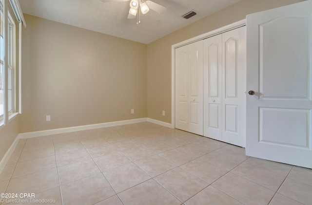 unfurnished bedroom with ceiling fan, a closet, light tile floors, and a textured ceiling