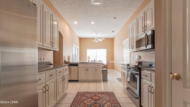 kitchen featuring kitchen peninsula, ceiling fan, light tile floors, appliances with stainless steel finishes, and a textured ceiling